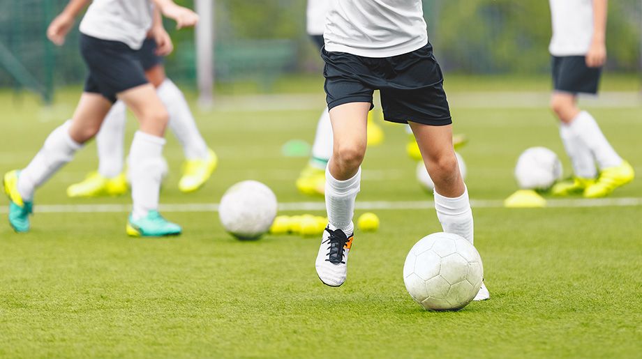 Kinder beim Fußballtraining mit Bällen auf einem grünen Kunstrasenplatz.