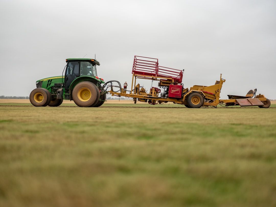 Grüner John Deere Traktor mit Spezialgerät zur Rasenpflege auf einem Sportplatz.