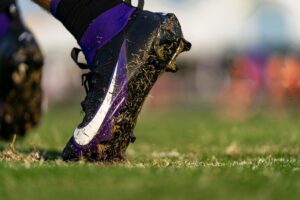 Verschmutzter violetter Fußballschuh hebt sich vom nassen Rasen ab