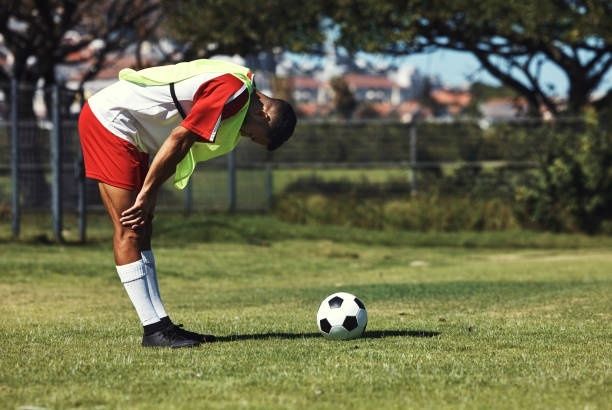 Erschöpfter Fußballspieler beugt sich auf dem Rasen über die Knie