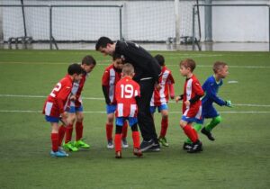 Junger Fußballtrainer spricht auf dem Spielfeld mit einer Kindergruppe