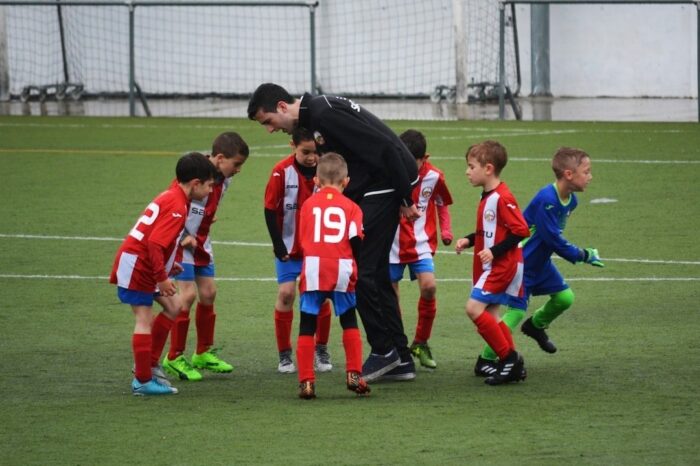 Junger Fußballtrainer spricht auf dem Spielfeld mit einer Kindergruppe