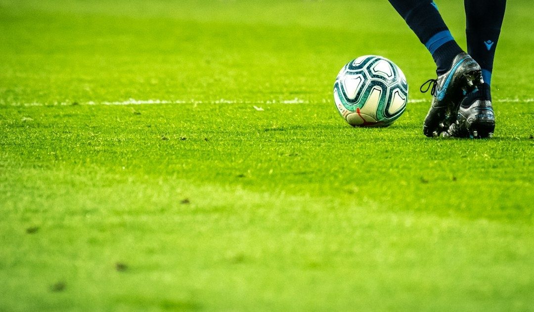 Fußballschuhe neben einem Ball auf dem grünen Spielfeld